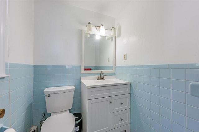 half bath with tile walls, a wainscoted wall, vanity, and toilet