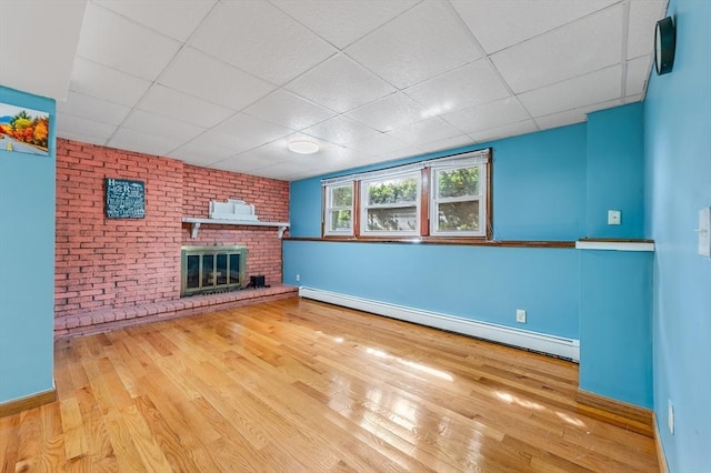 unfurnished living room with a baseboard radiator, wood finished floors, baseboards, a fireplace, and a paneled ceiling