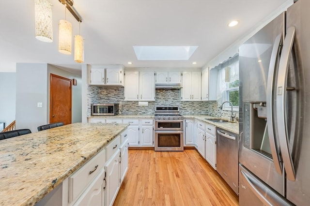 kitchen featuring appliances with stainless steel finishes, a sink, a skylight, white cabinets, and light wood-style floors