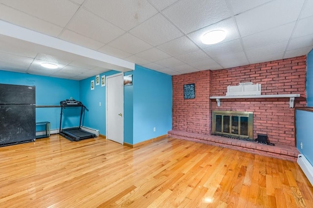 workout room with a paneled ceiling, wood finished floors, a fireplace, baseboards, and a baseboard heating unit
