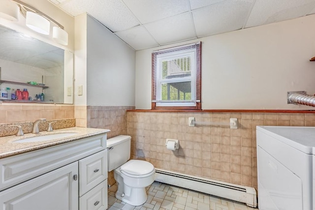 bathroom featuring a baseboard radiator, washer / clothes dryer, tile walls, toilet, and wainscoting