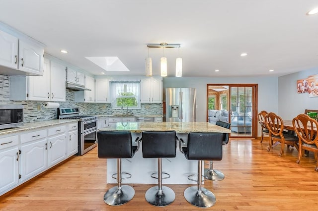 kitchen featuring stainless steel appliances, a skylight, under cabinet range hood, a sink, and white cabinetry