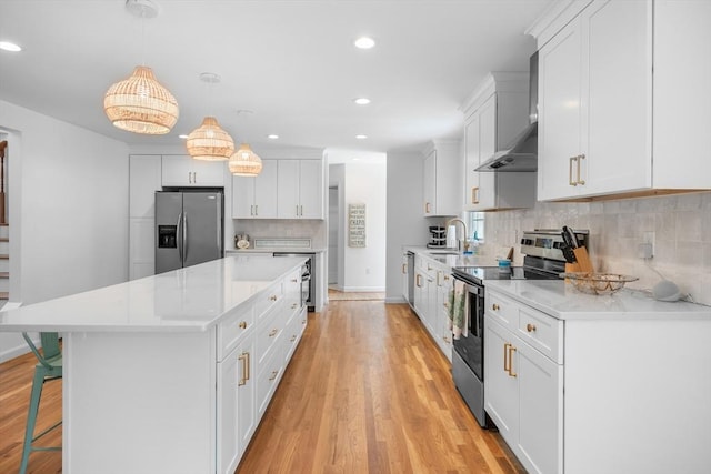 kitchen featuring stainless steel appliances, wall chimney range hood, recessed lighting, light wood finished floors, and light countertops