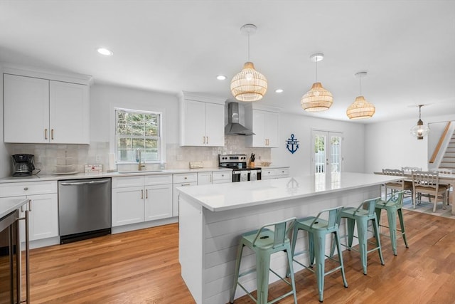 kitchen with appliances with stainless steel finishes, wall chimney exhaust hood, a sink, a breakfast bar, and french doors