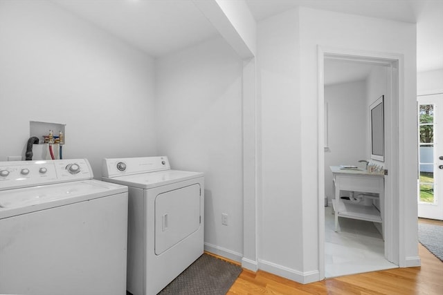 laundry room with washer and dryer, light wood finished floors, arched walkways, and baseboards