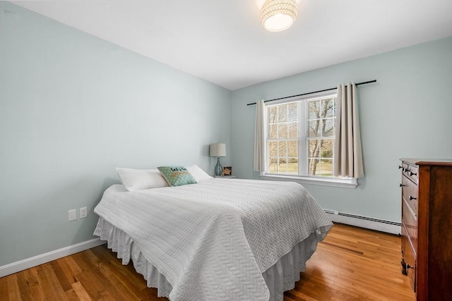 bedroom featuring a baseboard heating unit, wood finished floors, and baseboards