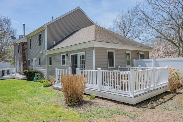 rear view of house featuring a wooden deck, a lawn, and a shingled roof