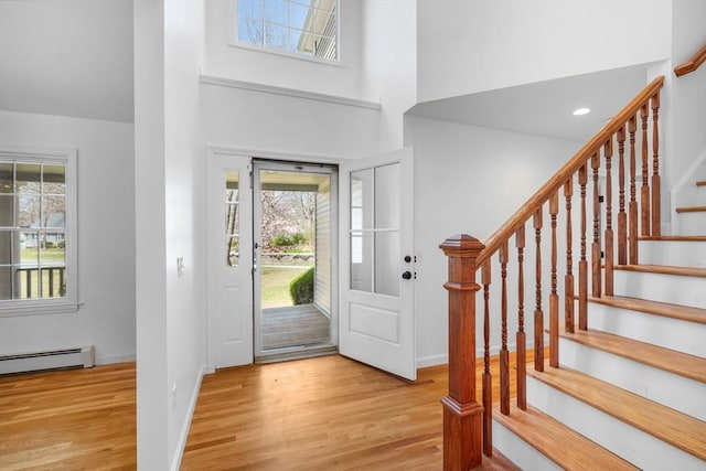 foyer entrance with plenty of natural light, wood finished floors, baseboard heating, stairs, and a high ceiling