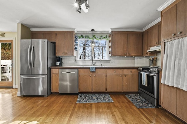 kitchen featuring appliances with stainless steel finishes, pendant lighting, sink, decorative backsplash, and light wood-type flooring