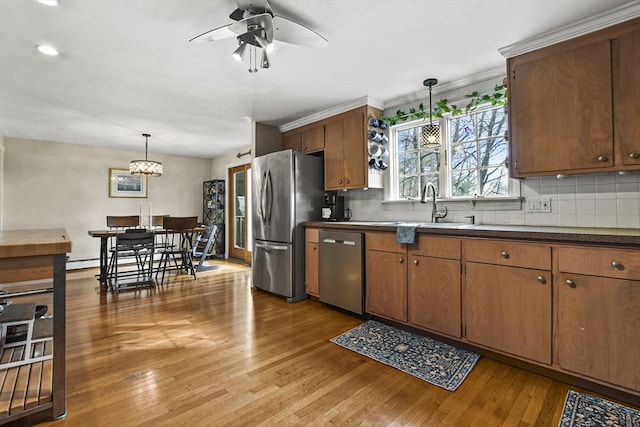 kitchen featuring sink, hanging light fixtures, light hardwood / wood-style flooring, appliances with stainless steel finishes, and decorative backsplash