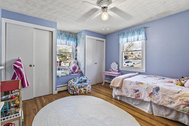 bedroom with multiple windows, a baseboard radiator, dark hardwood / wood-style floors, and two closets