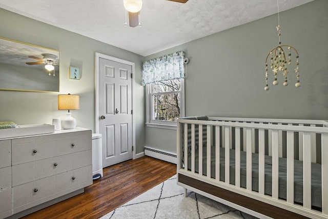 bedroom featuring dark hardwood / wood-style flooring, a nursery area, ceiling fan, and baseboard heating