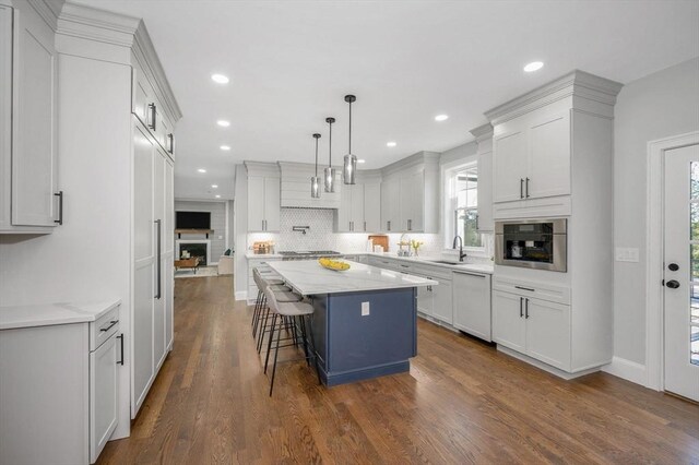 kitchen featuring hanging light fixtures, dark wood-type flooring, stainless steel appliances, a center island, and light stone countertops