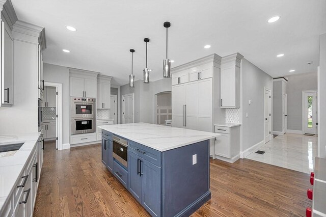 kitchen with light stone countertops, backsplash, appliances with stainless steel finishes, and dark hardwood / wood-style flooring