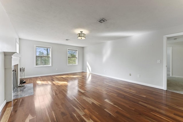 unfurnished living room featuring dark wood-style floors, visible vents, a fireplace with raised hearth, and baseboards