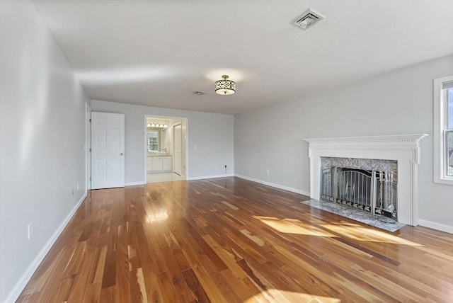 unfurnished living room featuring plenty of natural light, wood finished floors, visible vents, and a premium fireplace