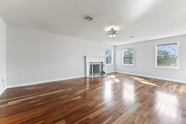 unfurnished living room with a fireplace, wood finished floors, visible vents, and baseboards