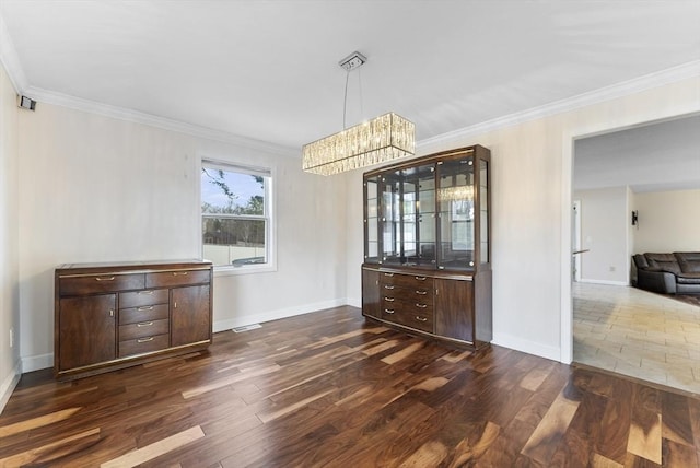 unfurnished dining area featuring visible vents, baseboards, dark wood finished floors, crown molding, and a chandelier