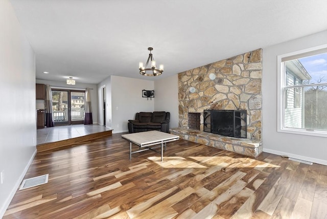 unfurnished living room featuring a stone fireplace, baseboards, visible vents, and wood finished floors