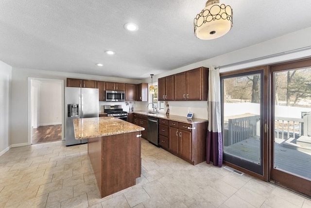 kitchen with visible vents, a center island, light stone counters, appliances with stainless steel finishes, and a sink