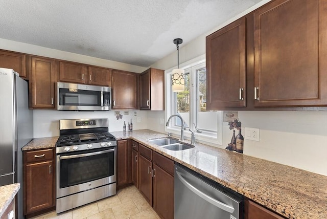 kitchen with pendant lighting, light stone counters, appliances with stainless steel finishes, a textured ceiling, and a sink