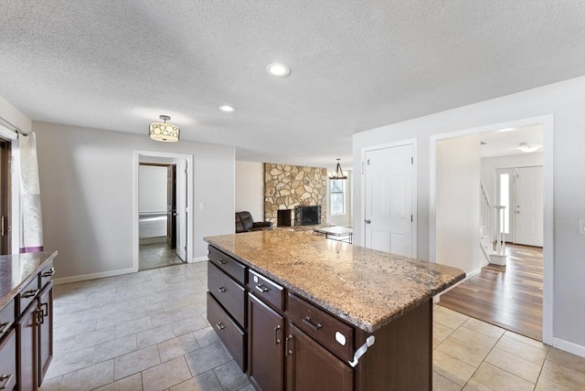 kitchen featuring light stone counters, a textured ceiling, a stone fireplace, and a center island