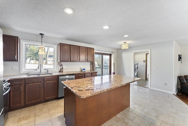 kitchen with light stone counters, a kitchen island, a sink, appliances with stainless steel finishes, and pendant lighting