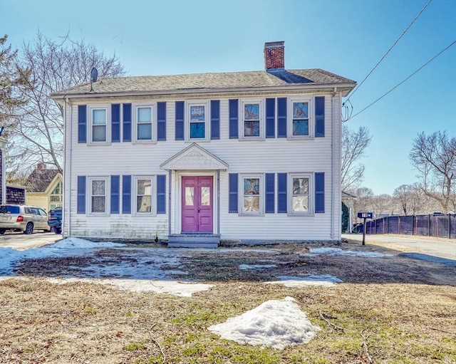 colonial house featuring a chimney and fence