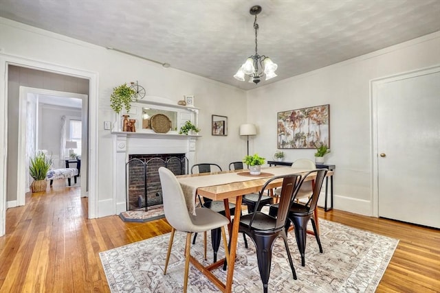 dining room featuring ornamental molding, a fireplace with raised hearth, light wood finished floors, and a chandelier