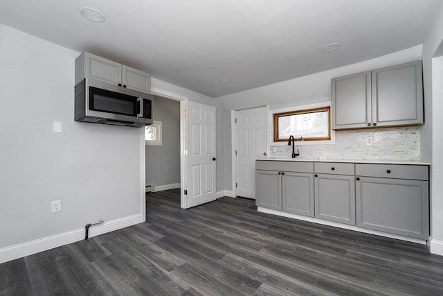 kitchen with gray cabinetry, dark wood-style flooring, a sink, backsplash, and stainless steel microwave