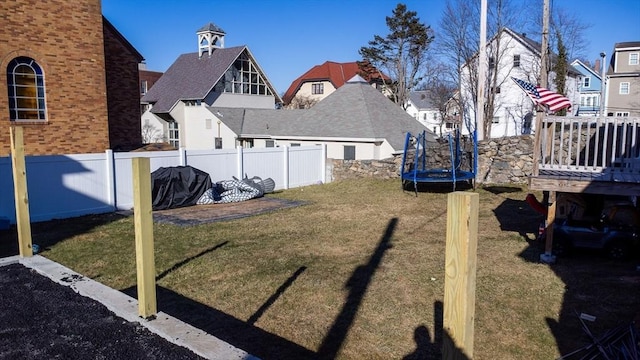 view of yard featuring a deck, a trampoline, a fenced backyard, and a residential view