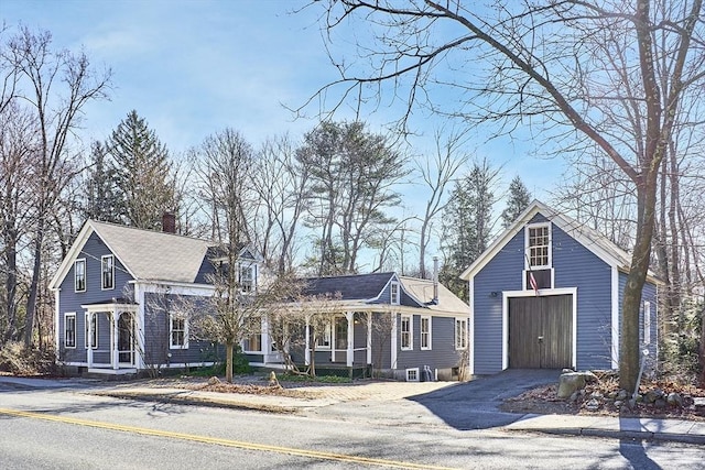 view of front facade featuring an outbuilding, driveway, a porch, a chimney, and a garage