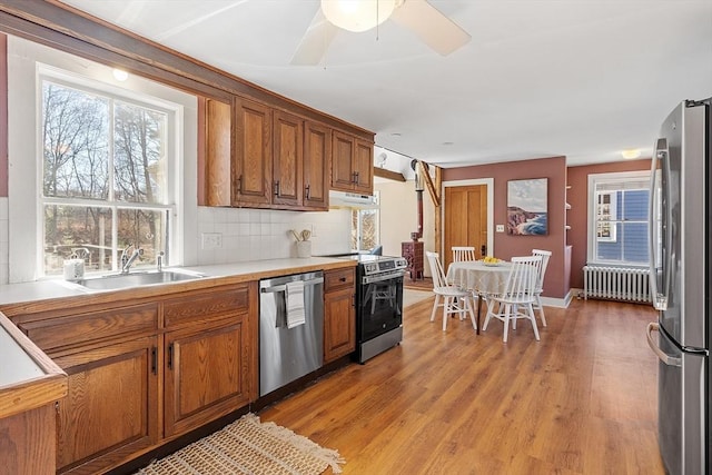 kitchen featuring light wood-type flooring, radiator heating unit, brown cabinetry, stainless steel appliances, and a sink