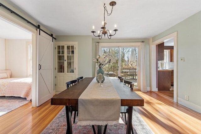 dining area with light wood finished floors, an inviting chandelier, baseboards, and a barn door