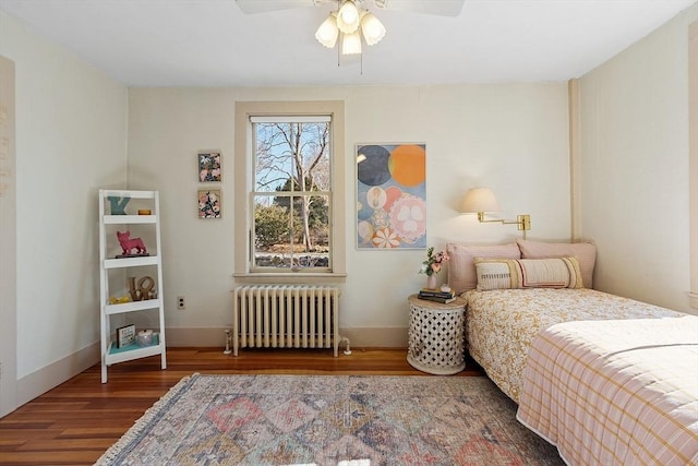 bedroom with ceiling fan, radiator heating unit, baseboards, and wood finished floors