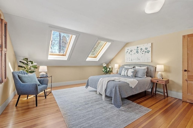 bedroom with baseboards, lofted ceiling with skylight, and light wood finished floors