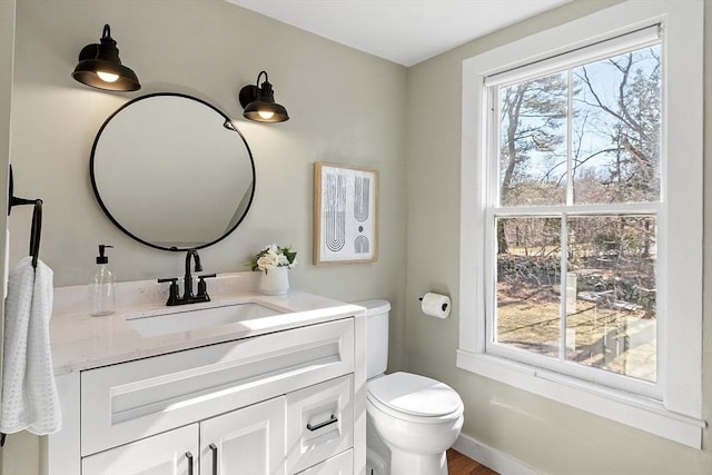 half bathroom with vanity, toilet, baseboards, and a wealth of natural light