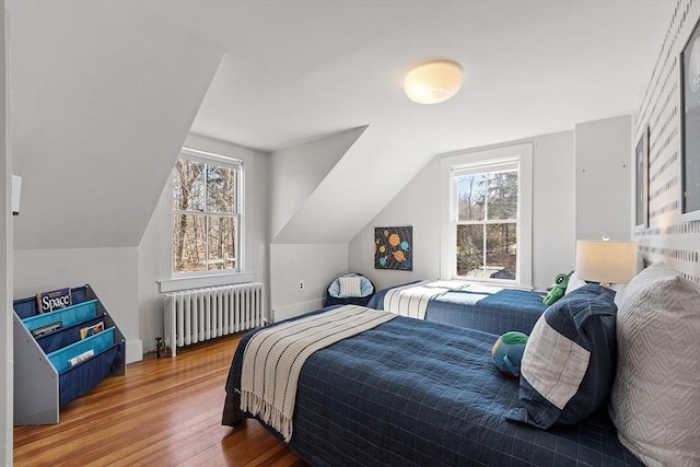 bedroom featuring lofted ceiling, multiple windows, radiator heating unit, and wood finished floors