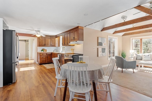 dining room featuring baseboards, beam ceiling, light wood-style flooring, ceiling fan, and a barn door