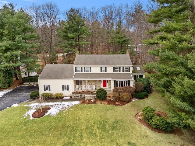 view of front of home with driveway, a chimney, a porch, and a front yard