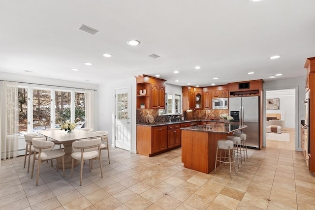 kitchen featuring visible vents, a breakfast bar area, stainless steel appliances, open shelves, and backsplash