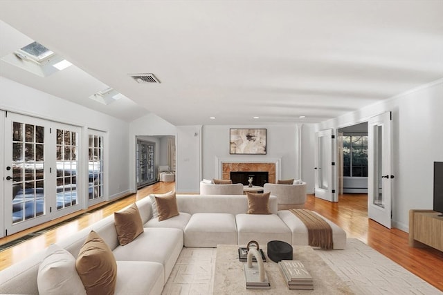 living room featuring vaulted ceiling with skylight, a fireplace, wood finished floors, visible vents, and baseboards