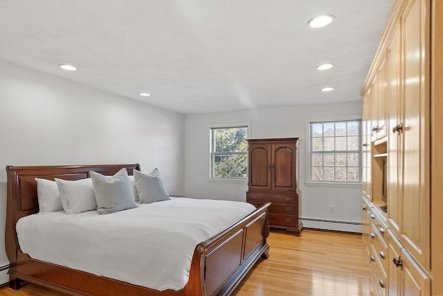 bedroom featuring multiple windows, baseboard heating, and light wood-style flooring