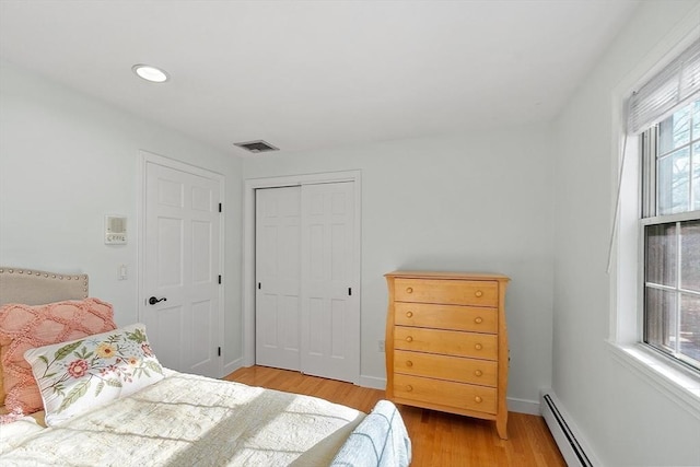 bedroom featuring visible vents, baseboards, light wood-style floors, a baseboard heating unit, and a closet