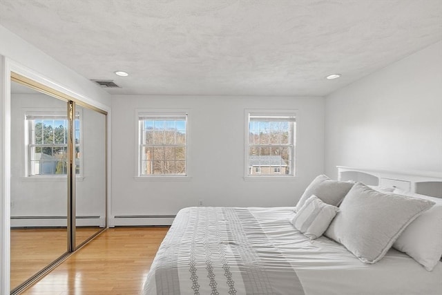 bedroom with multiple windows, baseboard heating, and light wood-style floors