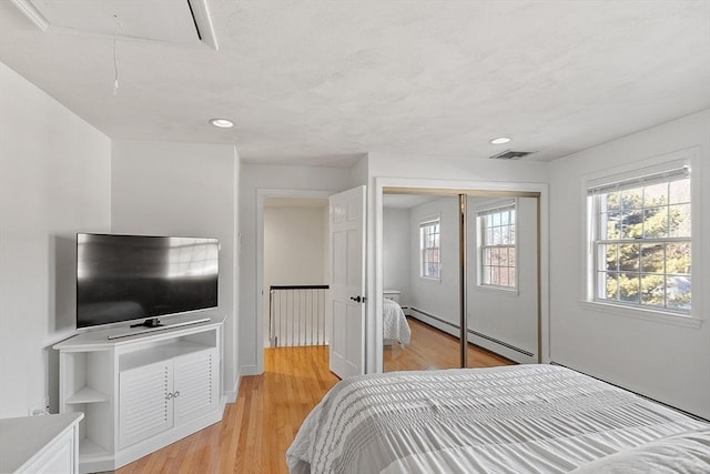 bedroom with light wood finished floors, a closet, visible vents, baseboard heating, and attic access