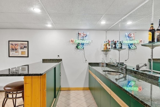 bar with indoor wet bar, a sink, a drop ceiling, and light tile patterned floors