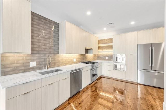 kitchen with premium appliances, sink, backsplash, light stone counters, and light hardwood / wood-style floors