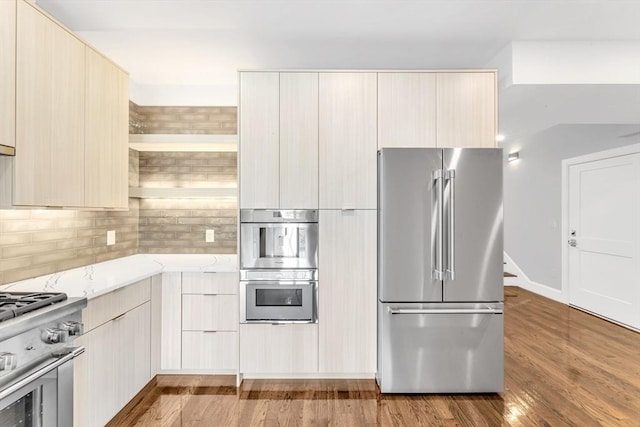 kitchen with light brown cabinetry, backsplash, premium appliances, and light wood-type flooring