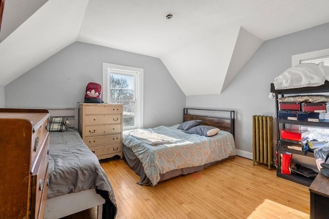 bedroom featuring lofted ceiling, radiator heating unit, and light hardwood / wood-style floors